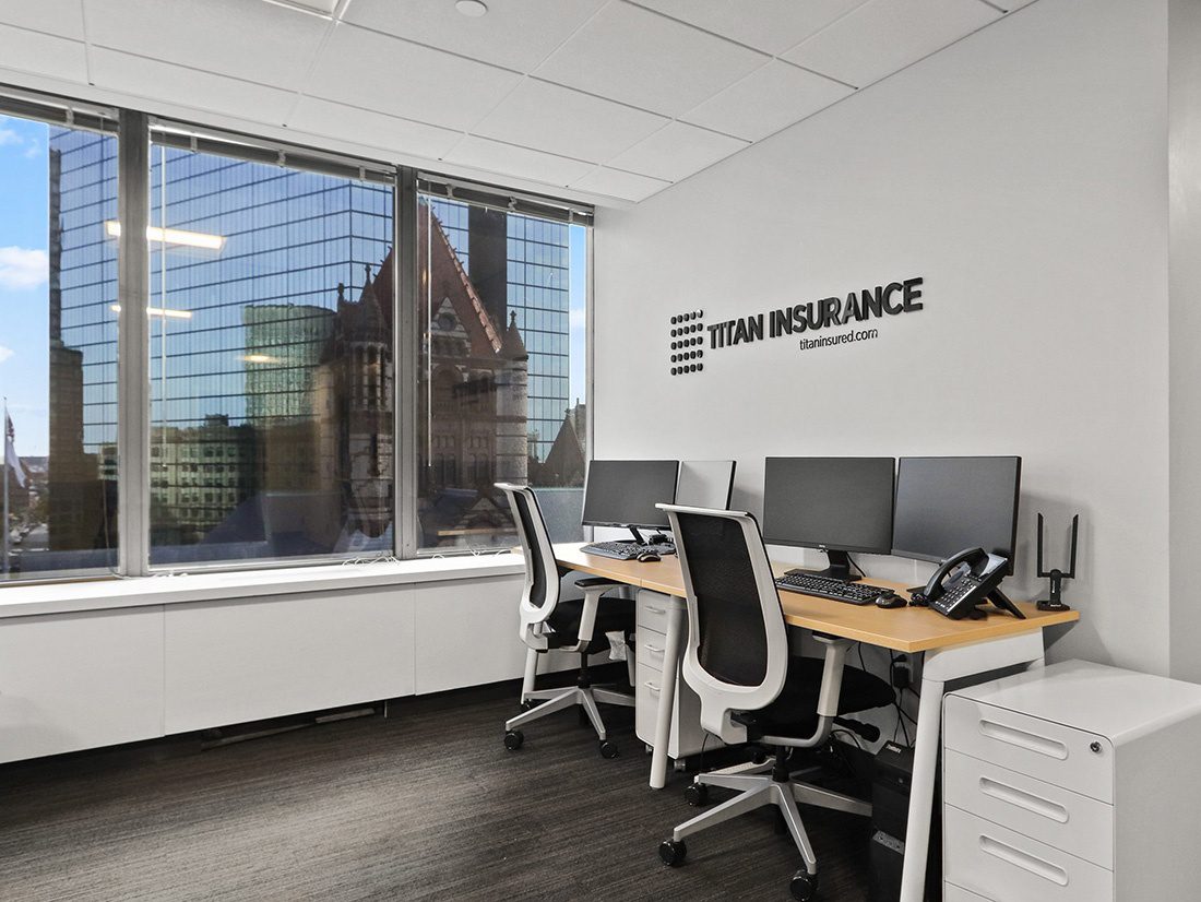 About Our Agency - View of Desks with Computers Next to a Wall in the Titan Insurance Office with a Logo Decal and Big Windows with Views of the City