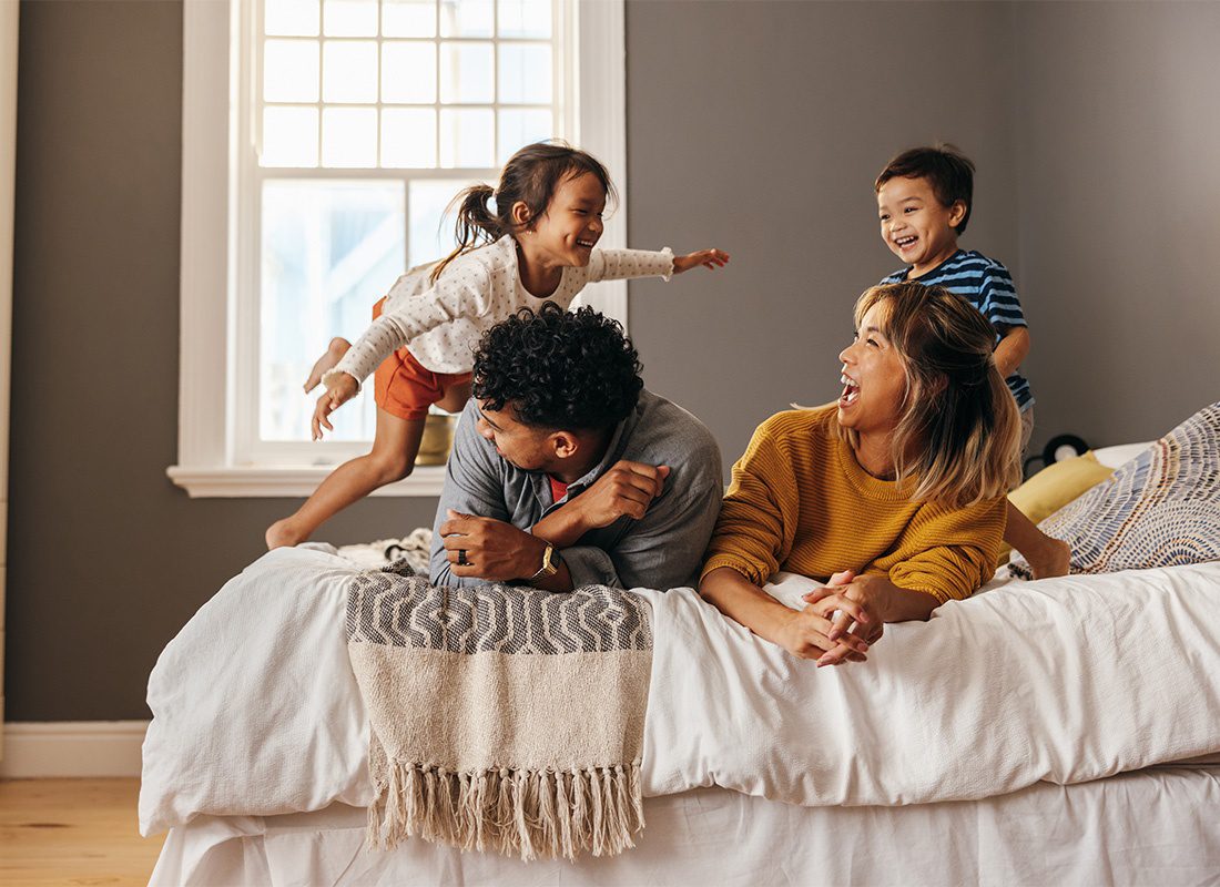 Personal Insurance - Portrait of Cheerful Young Parents with Two Children Having Fun Playing on the Bed at Home